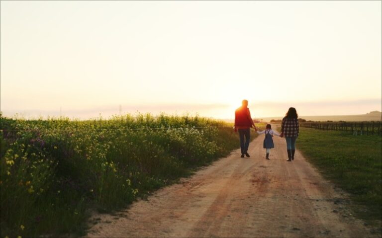 Family of 3 walking down a dirt road at sunset