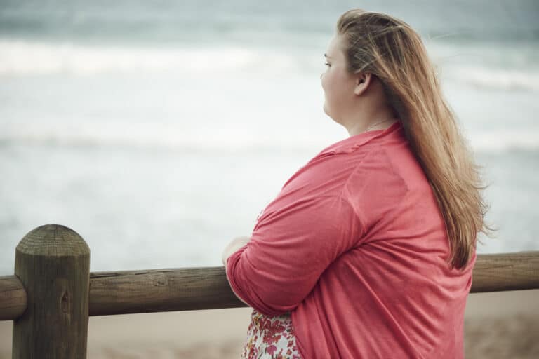 Overweight woman in pink shirt looking out at water