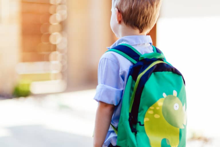 Little boy with green backpack walking to school