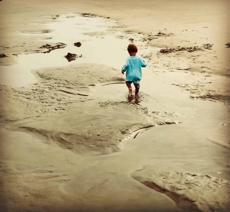 Little boy walking barefoot along sandy beach, color photo