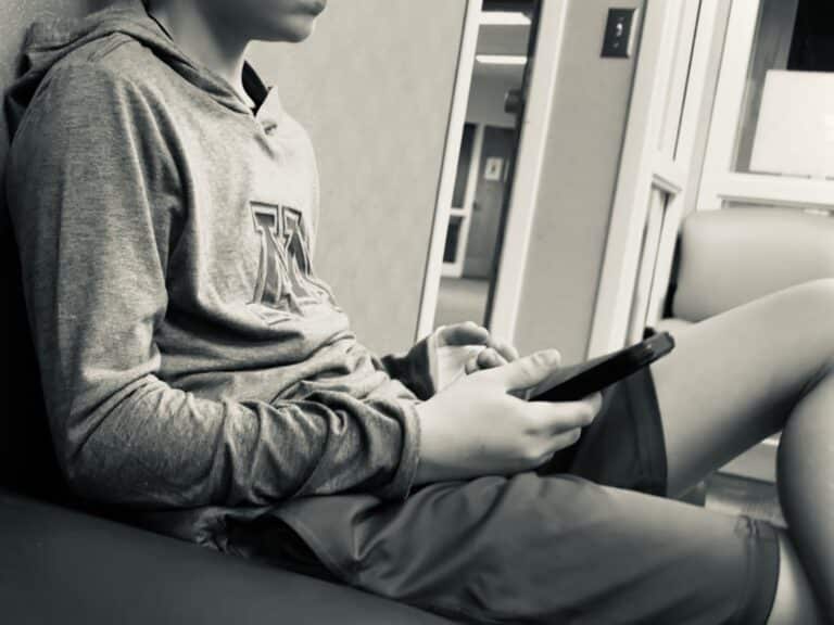 Tween holding smartphone and sitting in waiting room, black and white image