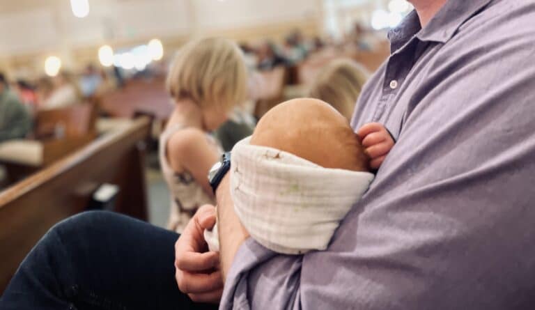 Close up of man holding baby in his arms in church pew with kids in background