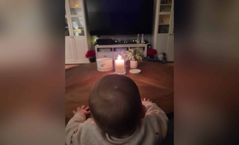 Toddler standing at table with lit candles, color photo