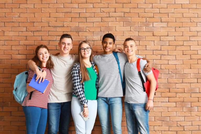 Teenagers with backpacks stand by brick wall