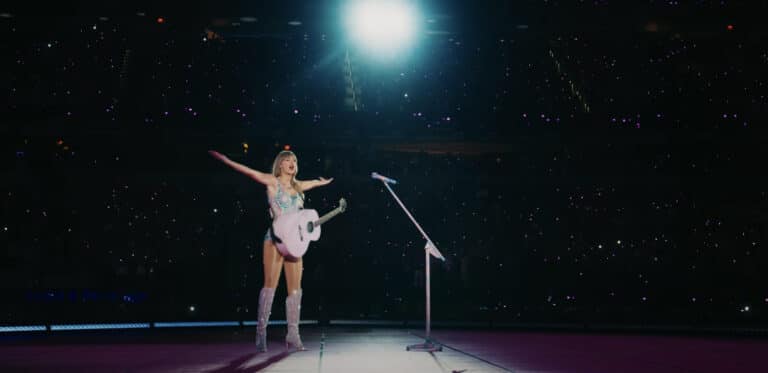 Taylor Swift The Eras Tour concert film official trailer still shot of female performer with guitar on stage under a spotlight