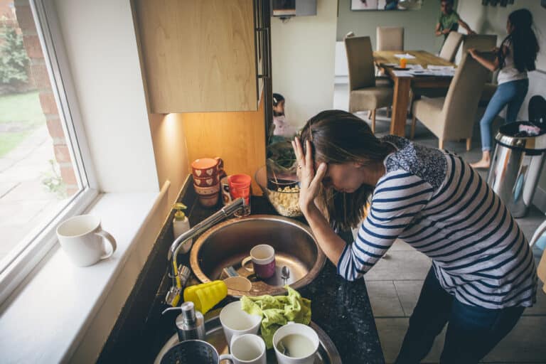 Stressed mother at home by kitchen sink with mess in background