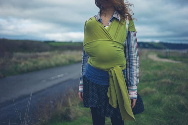 Mother with baby in green wrap standing by road
