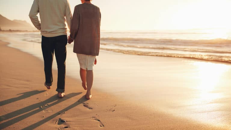 Older couple walking on beach holding hands