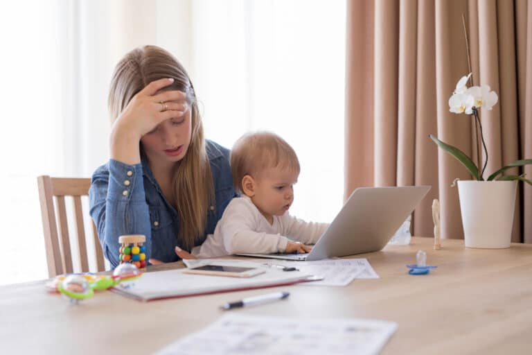 Stressed mother with papers and computer and a baby on her lap