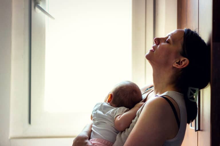 Woman holding newborn leaning against door with eyes closed