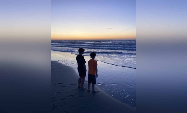 Two boys standing on shoreline, color photo