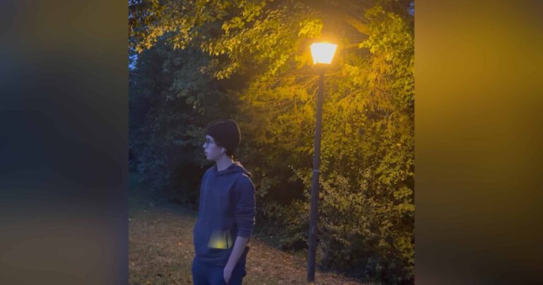 Teen boy standing near lamppost, color photo