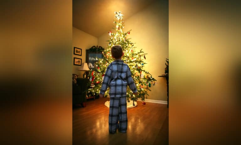Little boy standing in front of lit christmas tree