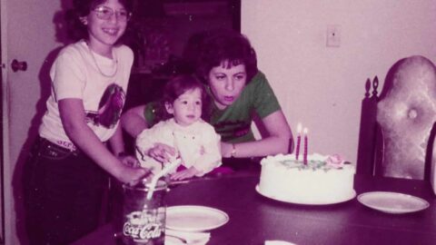 Older, color photo of mother and young daughter blowing out birthday candles