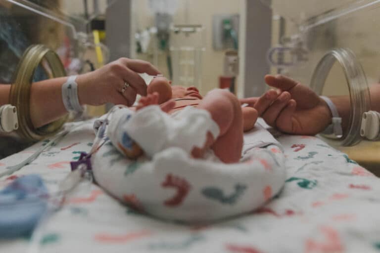 Parents holding hands of premature baby in NICU