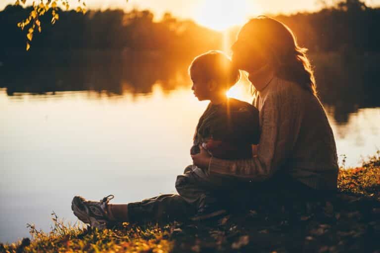 Mother sitting with child on her lap by the setting sun and water
