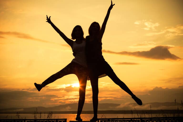 Two women embracing as silhouette in front of setting sun