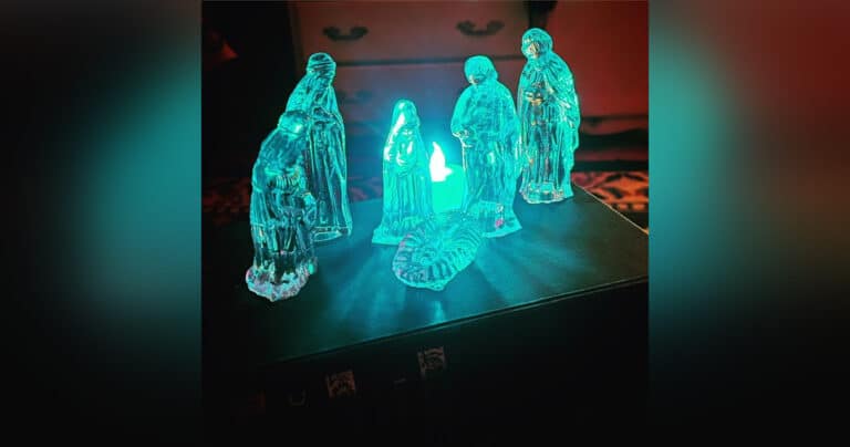 Crystal nativity set, glowing in front of blue tea light, color photo