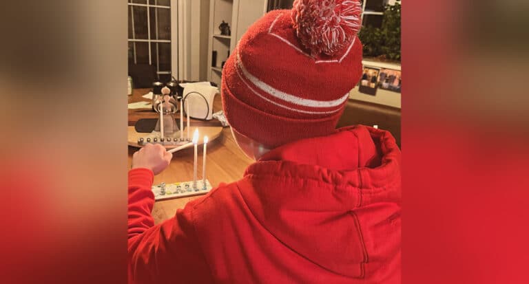 Child lighting a candle on a menorah, color photo