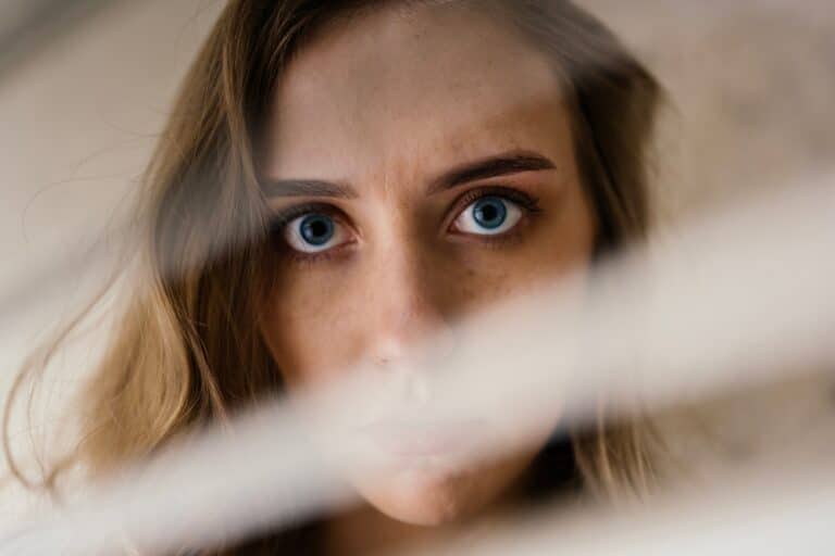 Woman hiding behind blinds with serious look