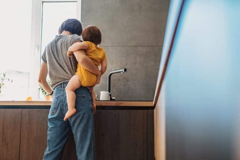 Mother standing at sink holding a baby on her hip
