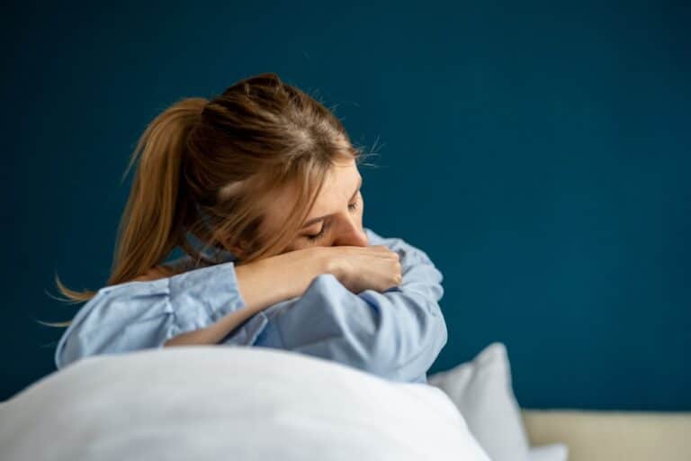 Sad woman with head in hands sitting on bed