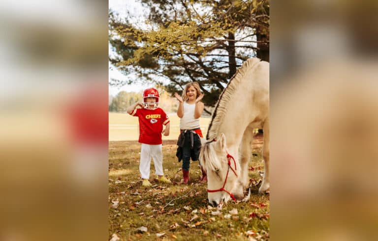 Kids dressed in Chiefs football uniform and Taylor Swift costumes standing outside by a horse, color photo