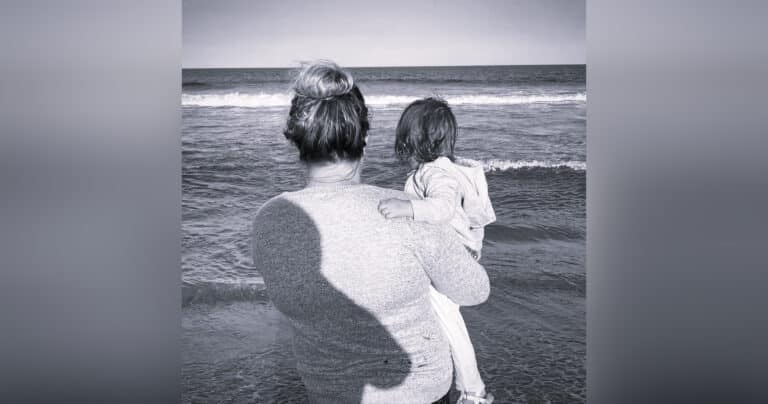 Woman holding child on the beach, black-and-white photo