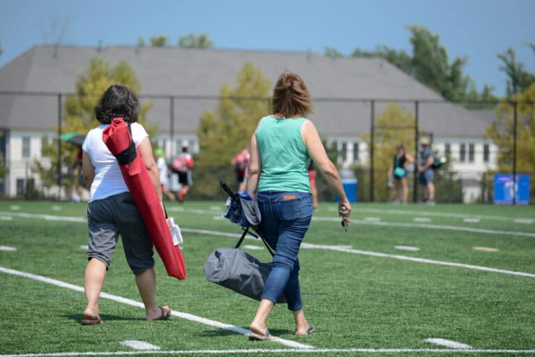 Sports parents walk across field carrying chair