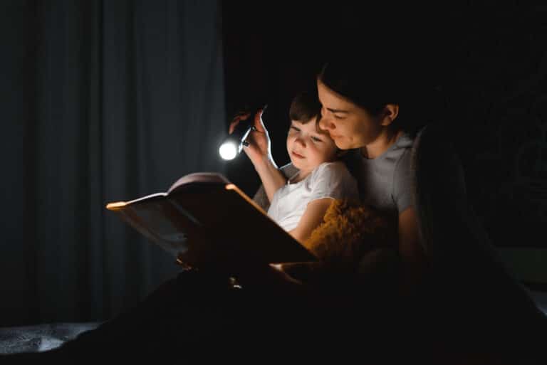 Mother reading to child at bedtime with flashlight
