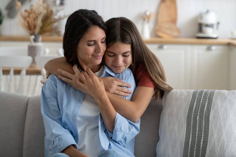 Mother and tween daughter hug on couch