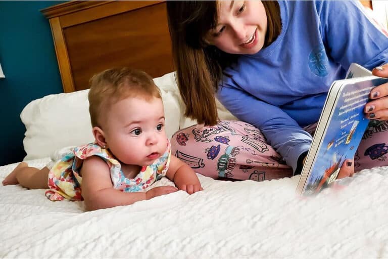 Mom with infant daughter on bed, reading a book, color photo