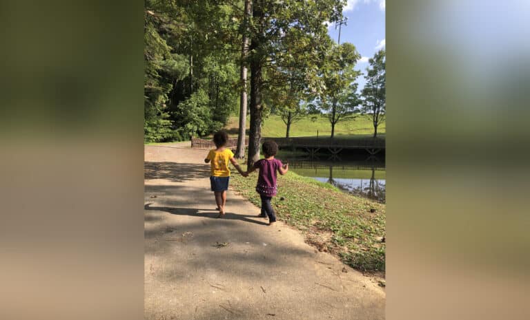 Two young children walking on a path near a pond, color photo
