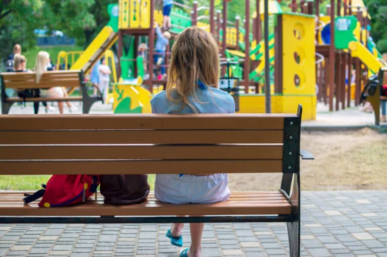Young mother sitting on bench looking at playground