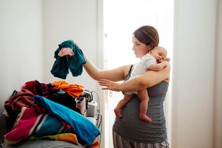 Woman holding baby sorting through laundry pile