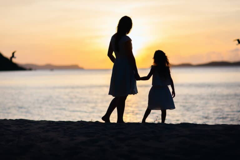 Mother and daughter hold hands by water, silhouette photo