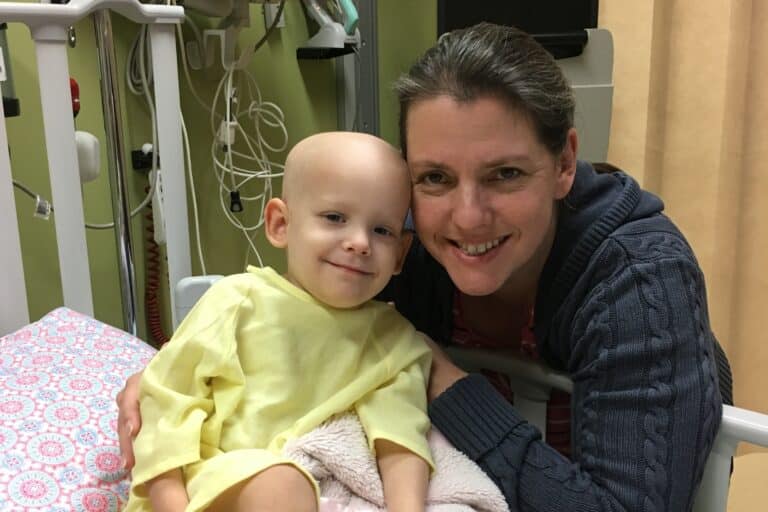 Bald-headed little girl in hospital bed with her mama, color photo