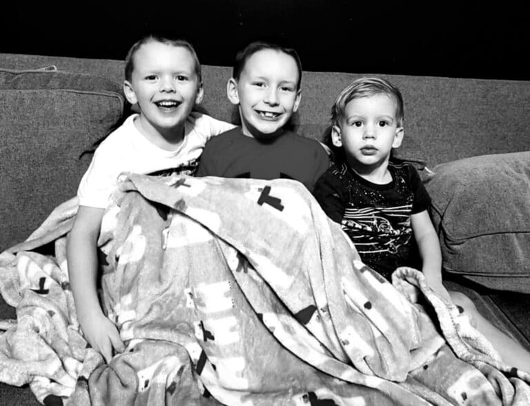 Three little boys under a blanket, black-and-white photo