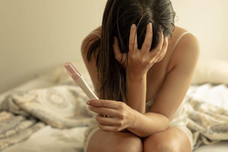 Woman sitting with pregnancy test sad