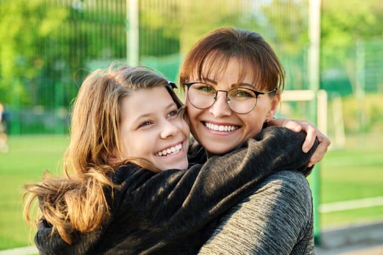 Mother with teen daughter embracing and smiling outside