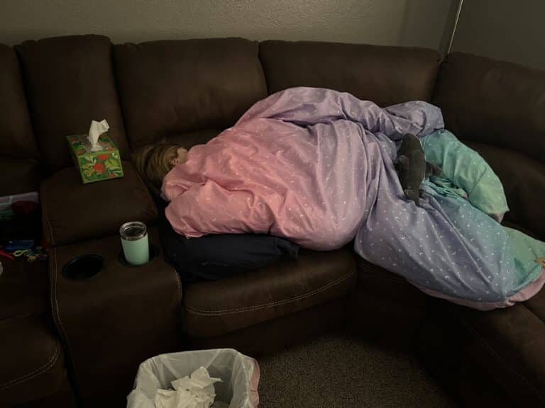 Child lying on couch under blankets, color photo