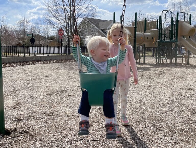 Little girl pushing toddler brother in baby swing, color photo
