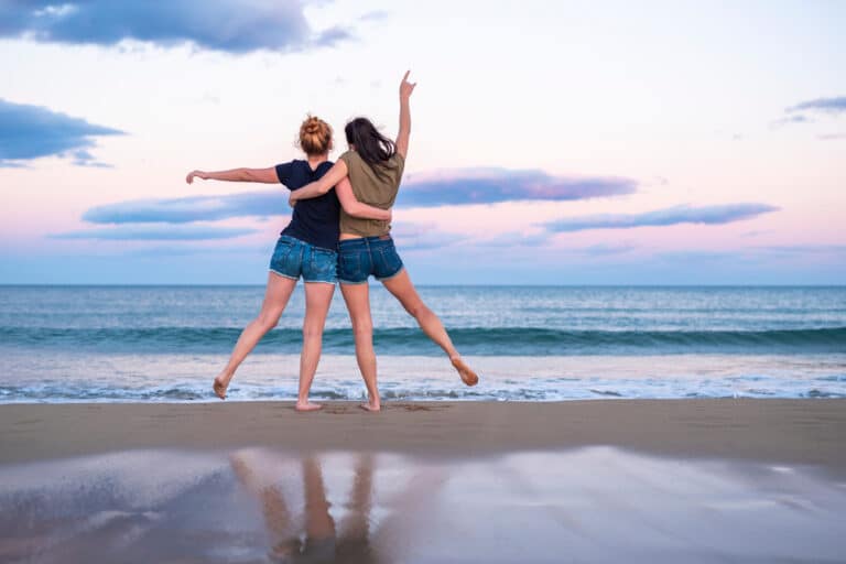 Two friends standing at ocean's edge with arms around each other