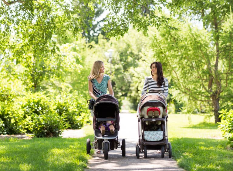 Two mothers push strollers outside