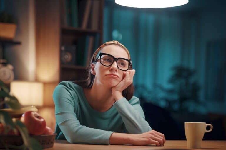 Exhausted woman wearing glasses sitting at kitchen table