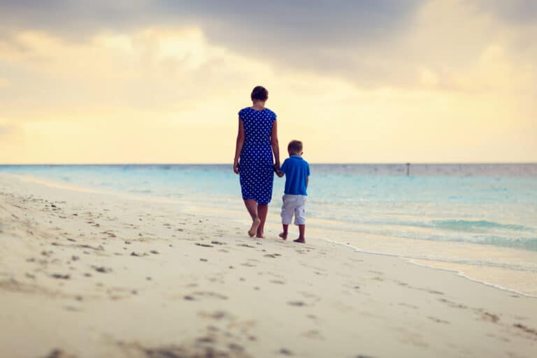 Mother and son walk along beach holding hands
