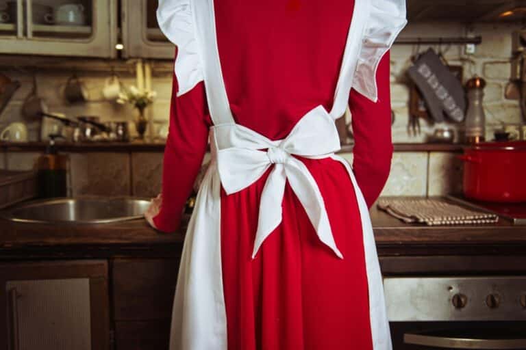 Woman standing at stove wearing apron tied over red dress