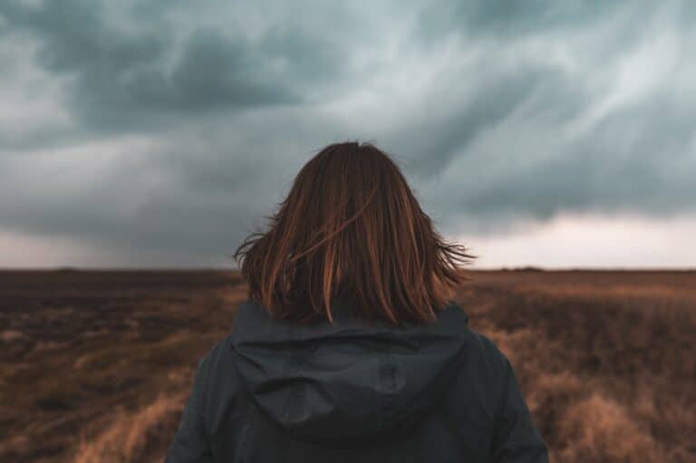 Woman standing in front of storm clouds and barren field
