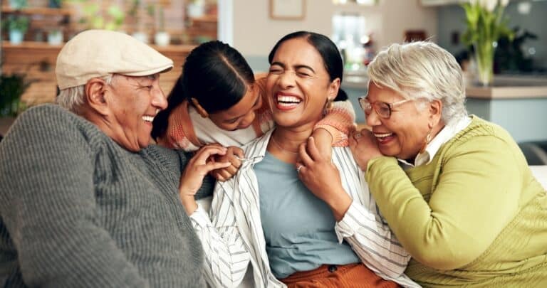 Grandparents with child and grown daughter smiling and laughing on couch