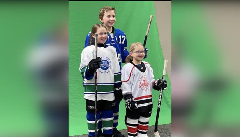 Three youth hockey players standing with hockey sticks smiling at camera